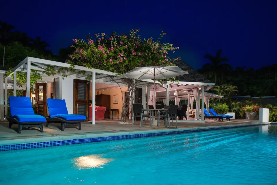 Night view of a Signature Villa pool terrace at Round Hill Hotel And Villas with blue loungers and umbrellas.