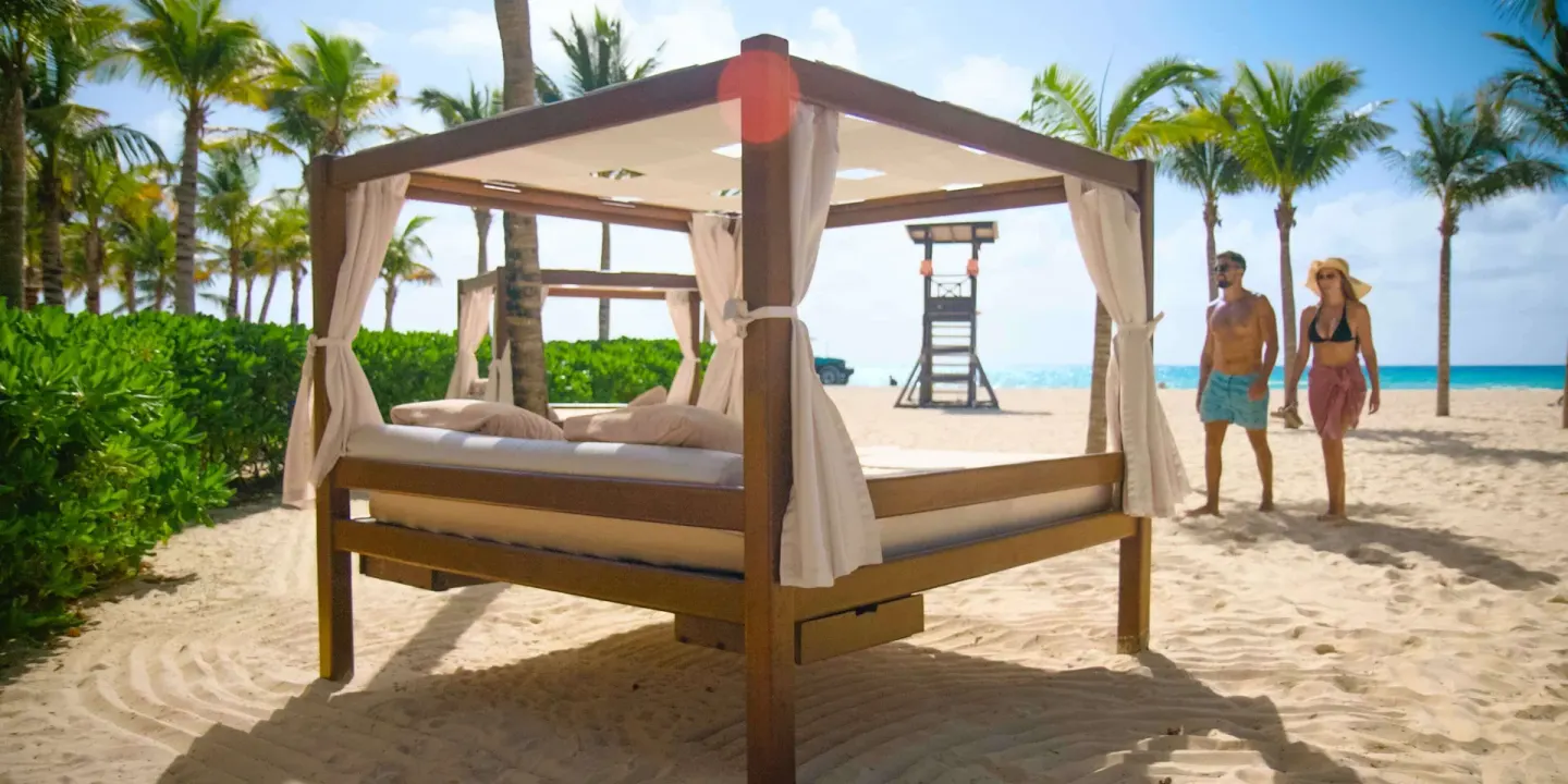 Beach cabana with curtains on the sand at Royal Hideaway Playacar, with palms and ocean beyond.