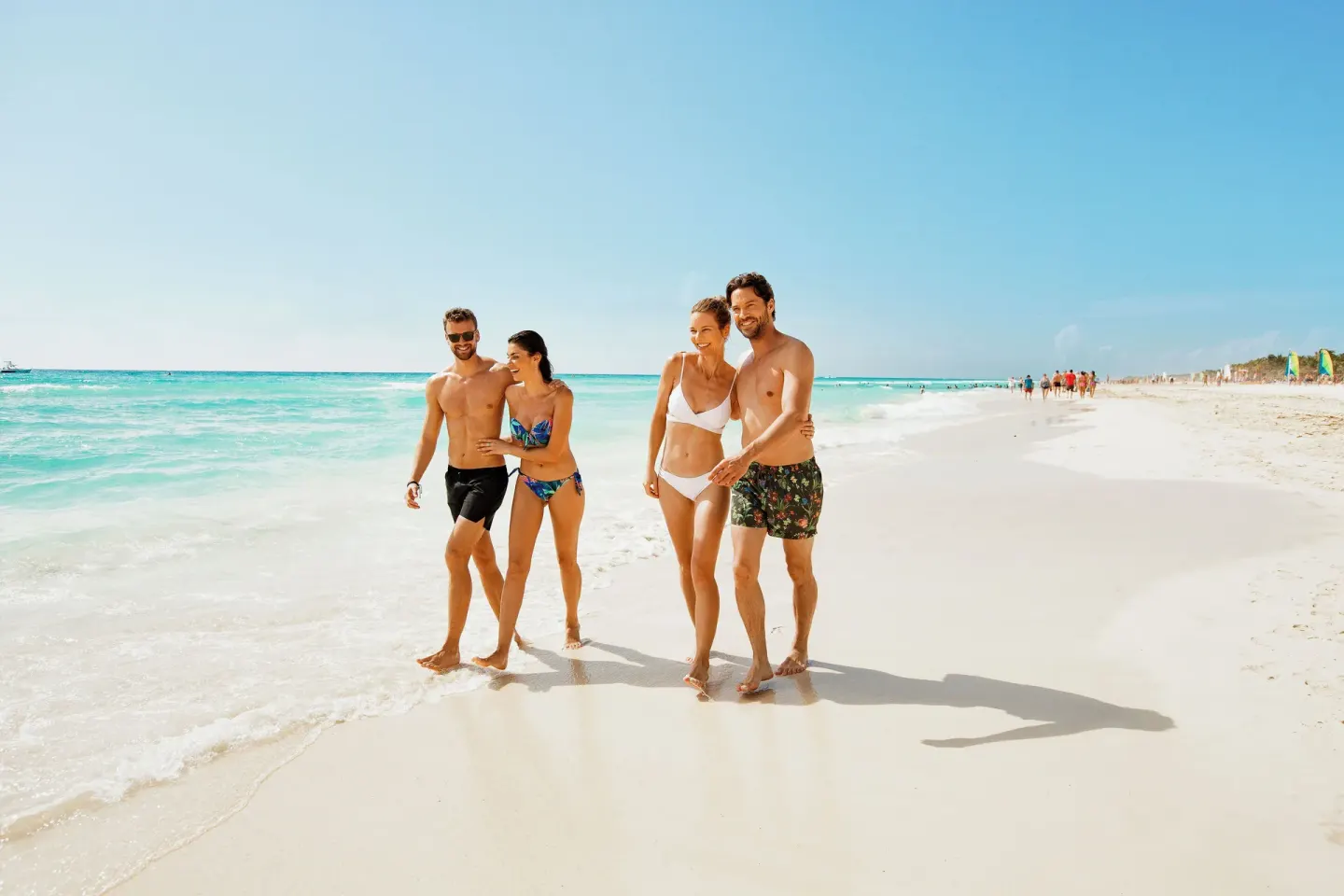 Guests walking along the shoreline by turquoise water at Royal Hideaway Playacar.