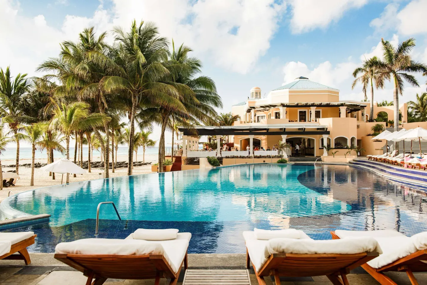 Beachfront pool with palm trees and loungers at Royal Hideaway Playacar.