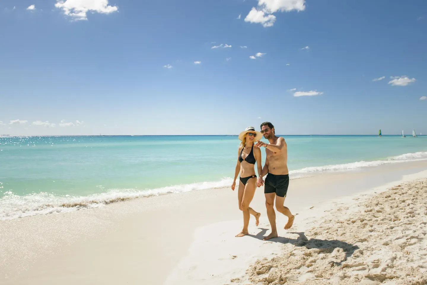 Couple walks along the shoreline beside clear turquoise water at Royal Hideaway Playacar.
