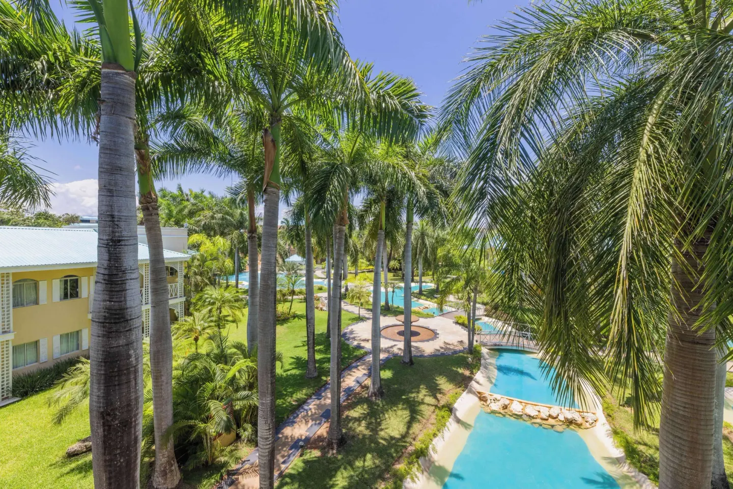 Palm-lined view of pools and gardens from a Luxury Royal Hideaway Playacar at Royal Hideaway Playacar.