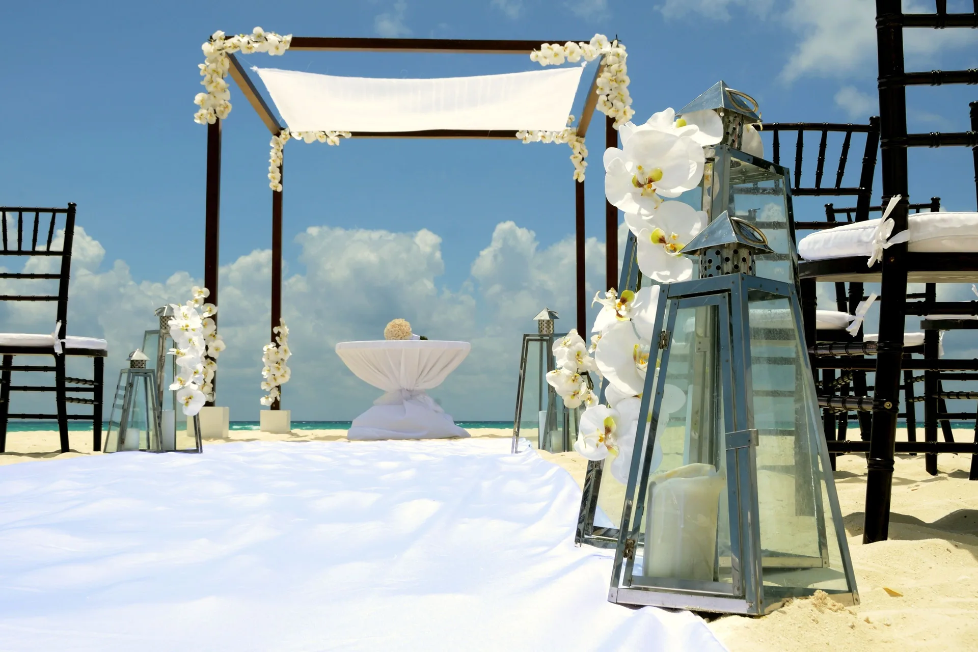 Beach wedding ceremony setup with floral arch and lanterns at Royal Hideaway Playacar.