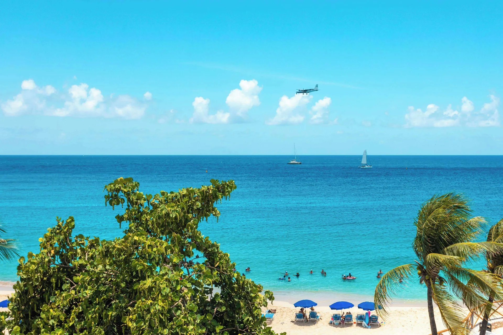 Beach and turquoise sea with swimmers and sailboats at Royal Islander Resort La Plage.
