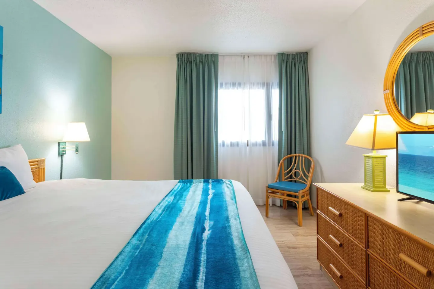Guest bedroom with king bed, wicker dresser, and chair at Royal Islander Resort La Plage.
