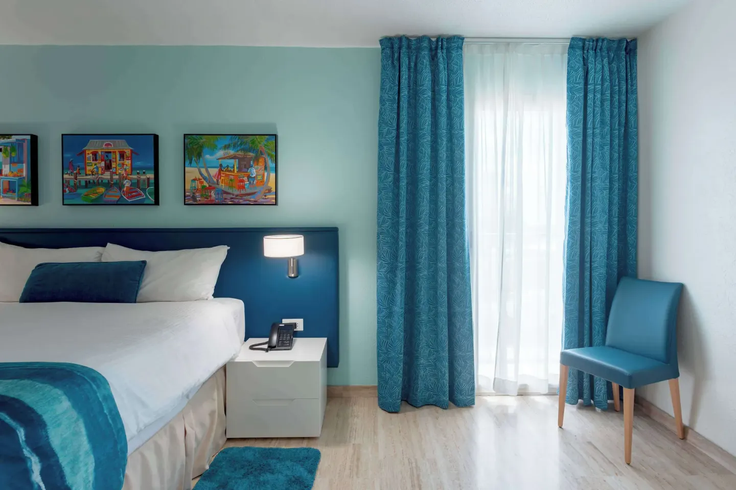 Blue-accent guest room with bed and balcony curtains at Royal Islander Resort La Plage.