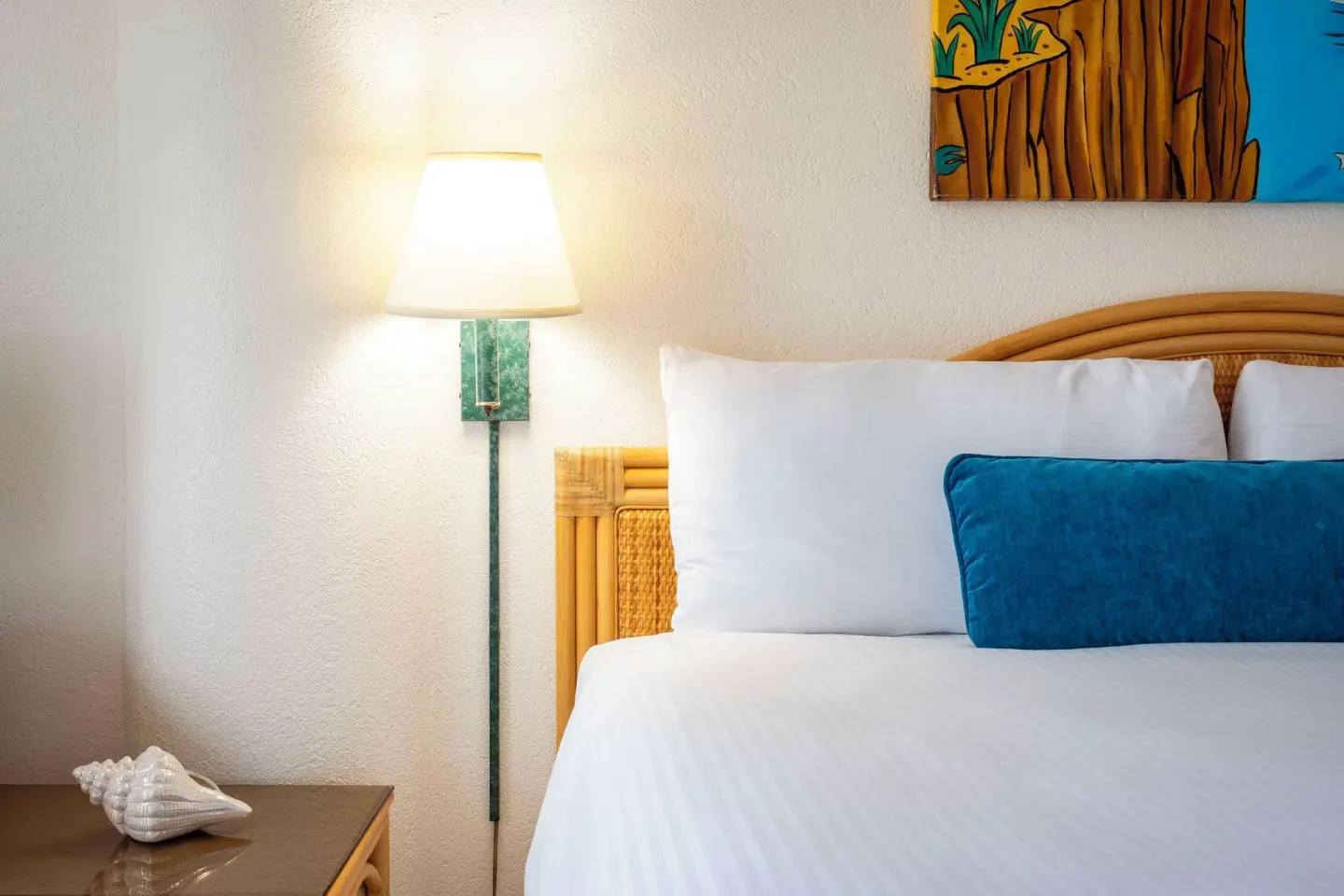 Close-up of a guest room bed and bedside lamp at Royal Islander Resort La Plage.