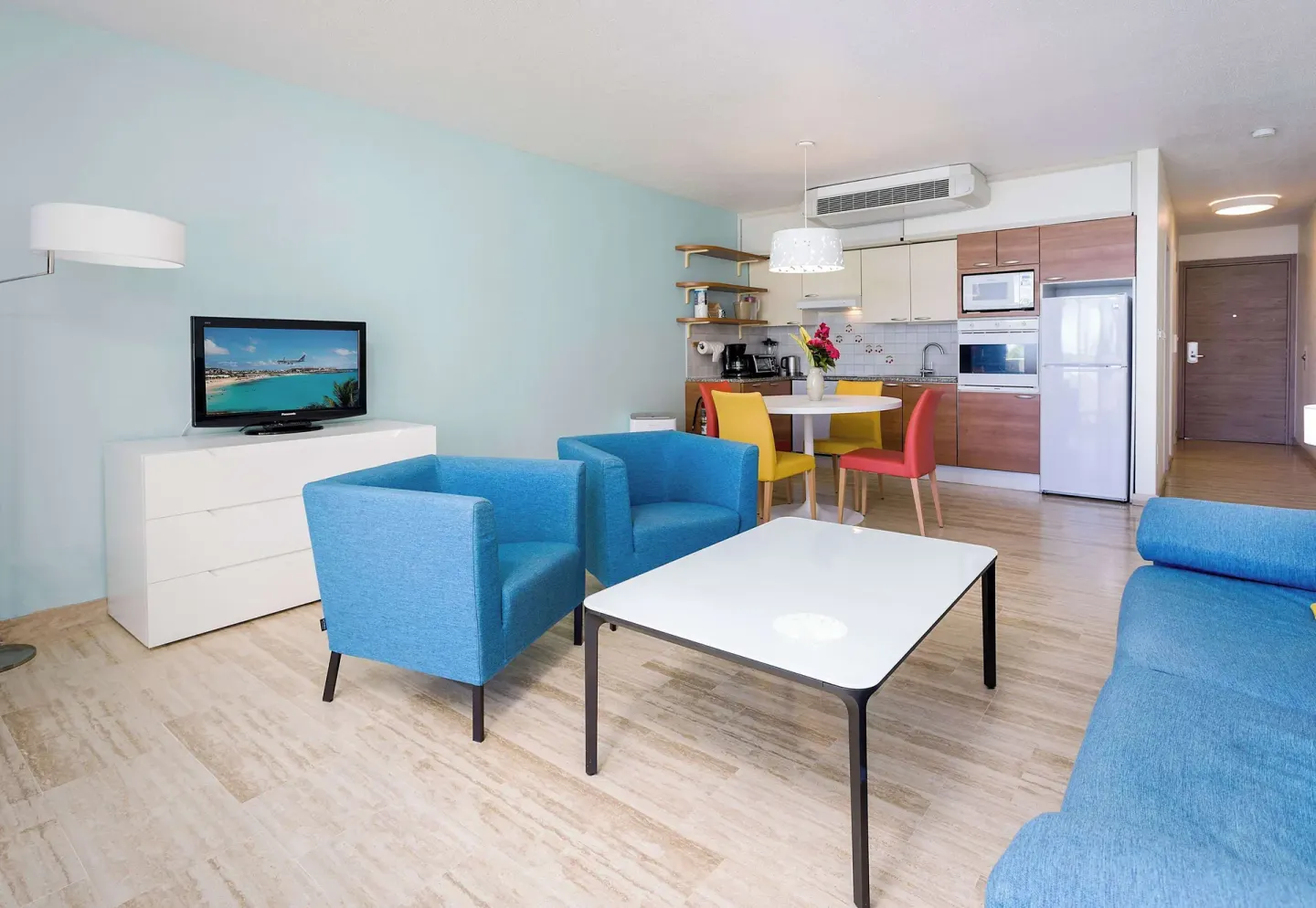 Suite living room with blue chairs, TV, and kitchenette at Royal Islander Resort La Plage.