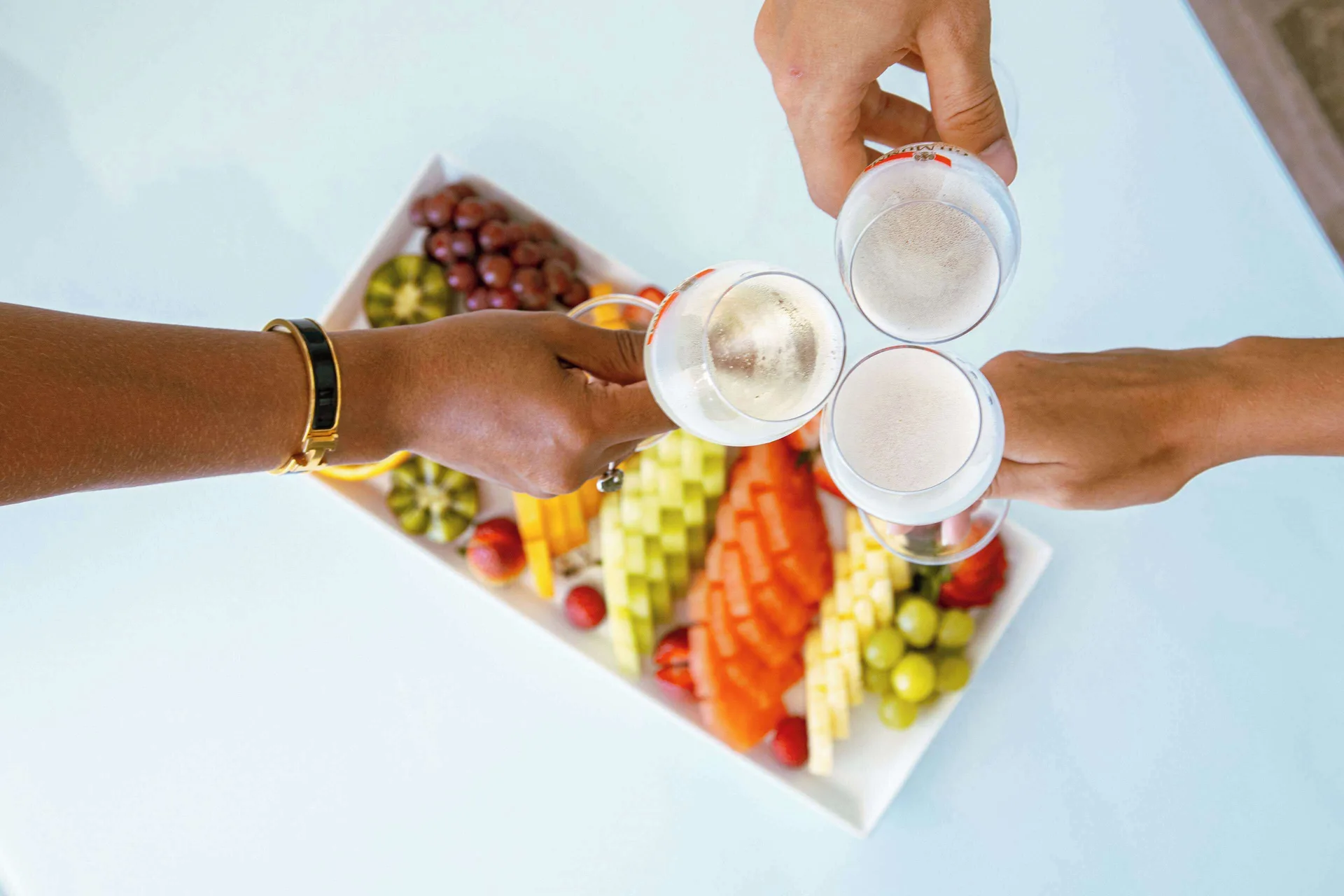 Hands toast sparkling drinks over a fruit platter at Royal Islander Resort La Plage.