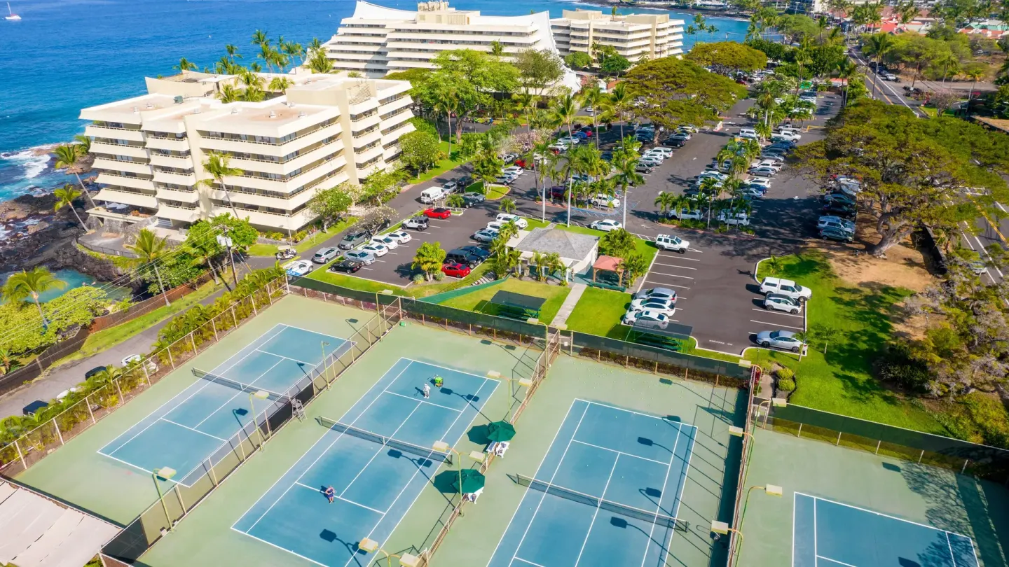 Aerial view of tennis courts, resort buildings, parking, and ocean at Royal Kona Resort.