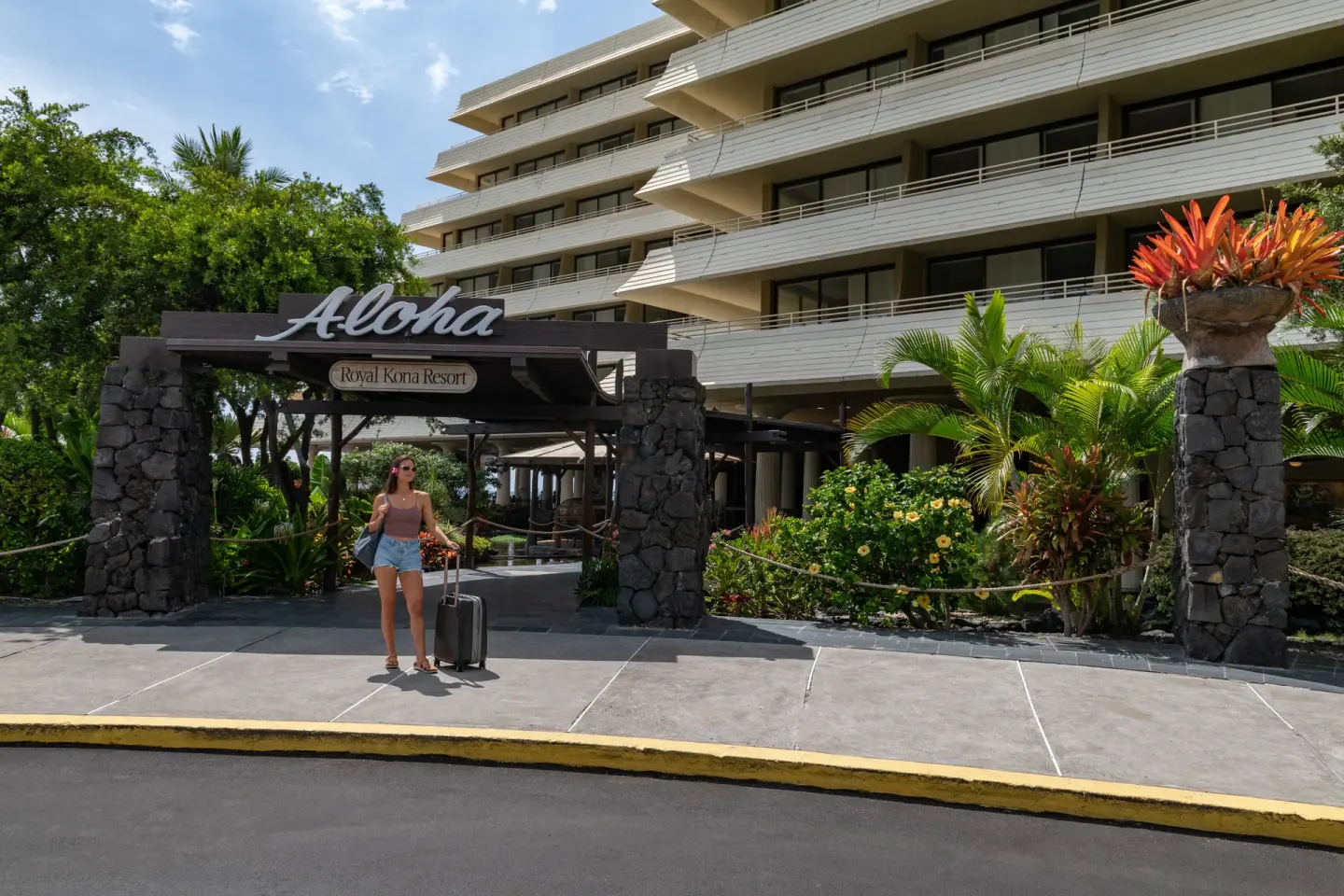 Entrance sign and resort tower with guest arriving at Royal Kona Resort.