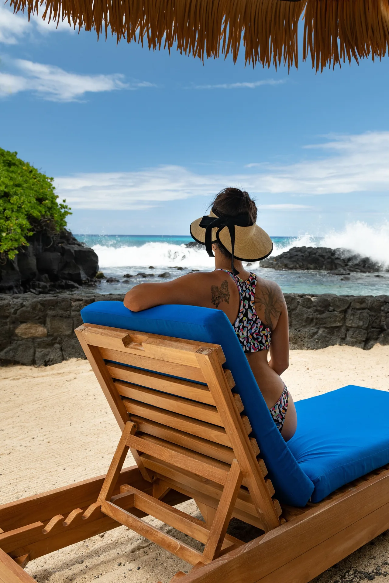 A blue-cushioned lounge chair faces the surf and lava rocks at Royal Kona Resort.