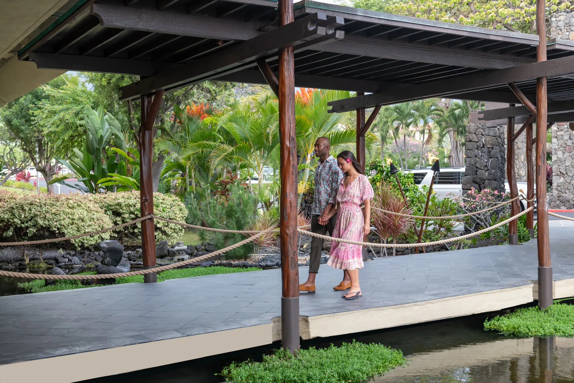 Couple walking on a covered garden bridge over water at Royal Kona Resort.