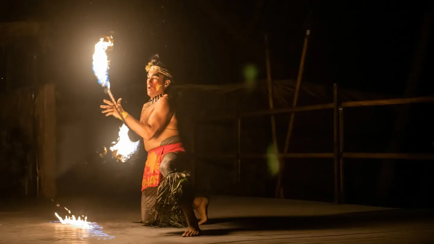 Fire dancer kneels onstage with a flaming torch during a night show at Royal Kona Resort.
