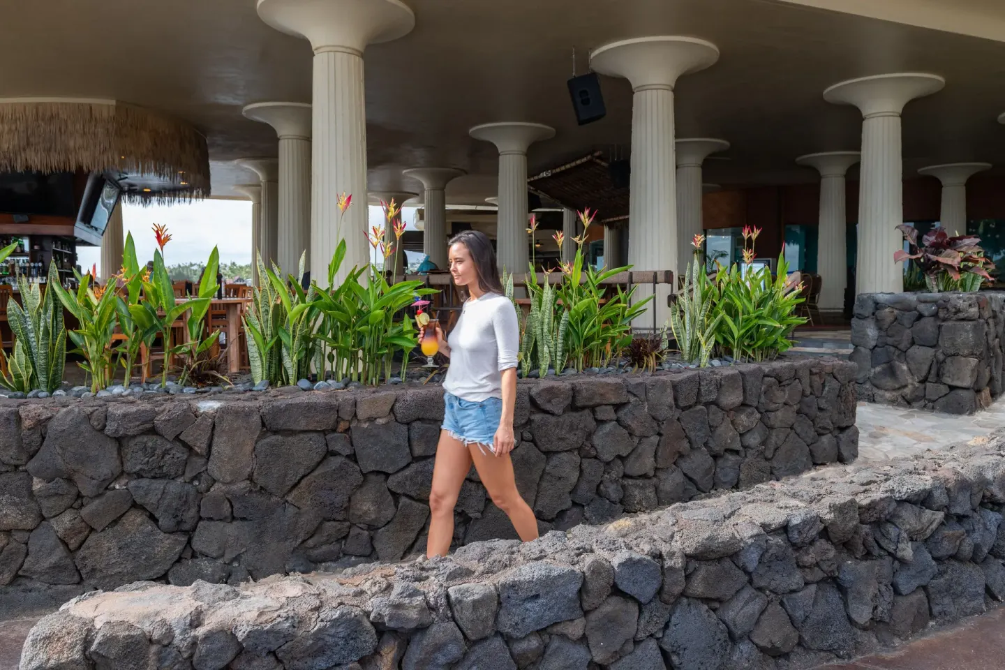 Guest walks with a tropical drink past lava-rock planters at Royal Kona Resort.