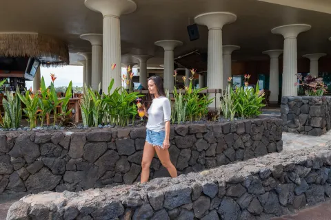 Guest walks with a tropical drink past lava-rock planters at Royal Kona Resort.