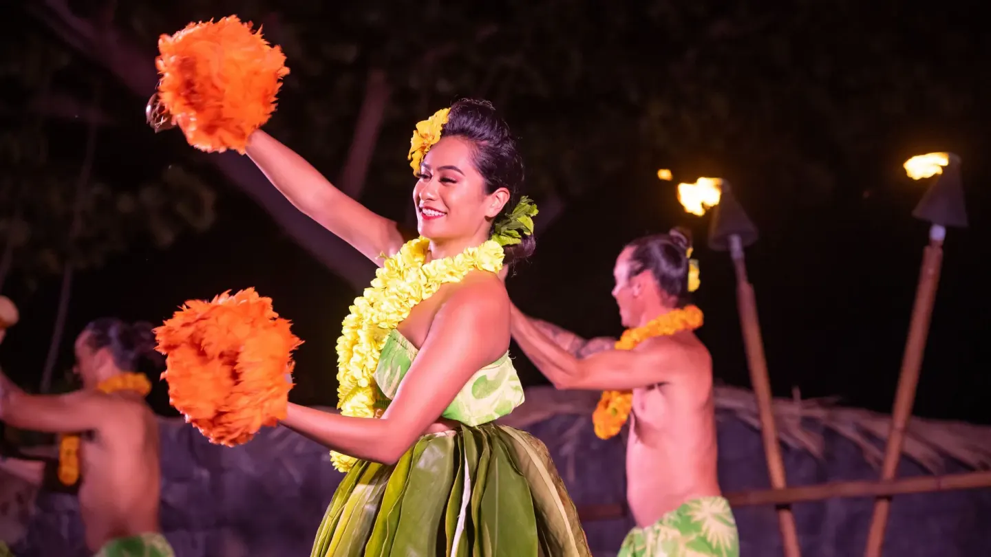 Hula dancers perform at night with torches and orange feather implements at Royal Kona Resort.