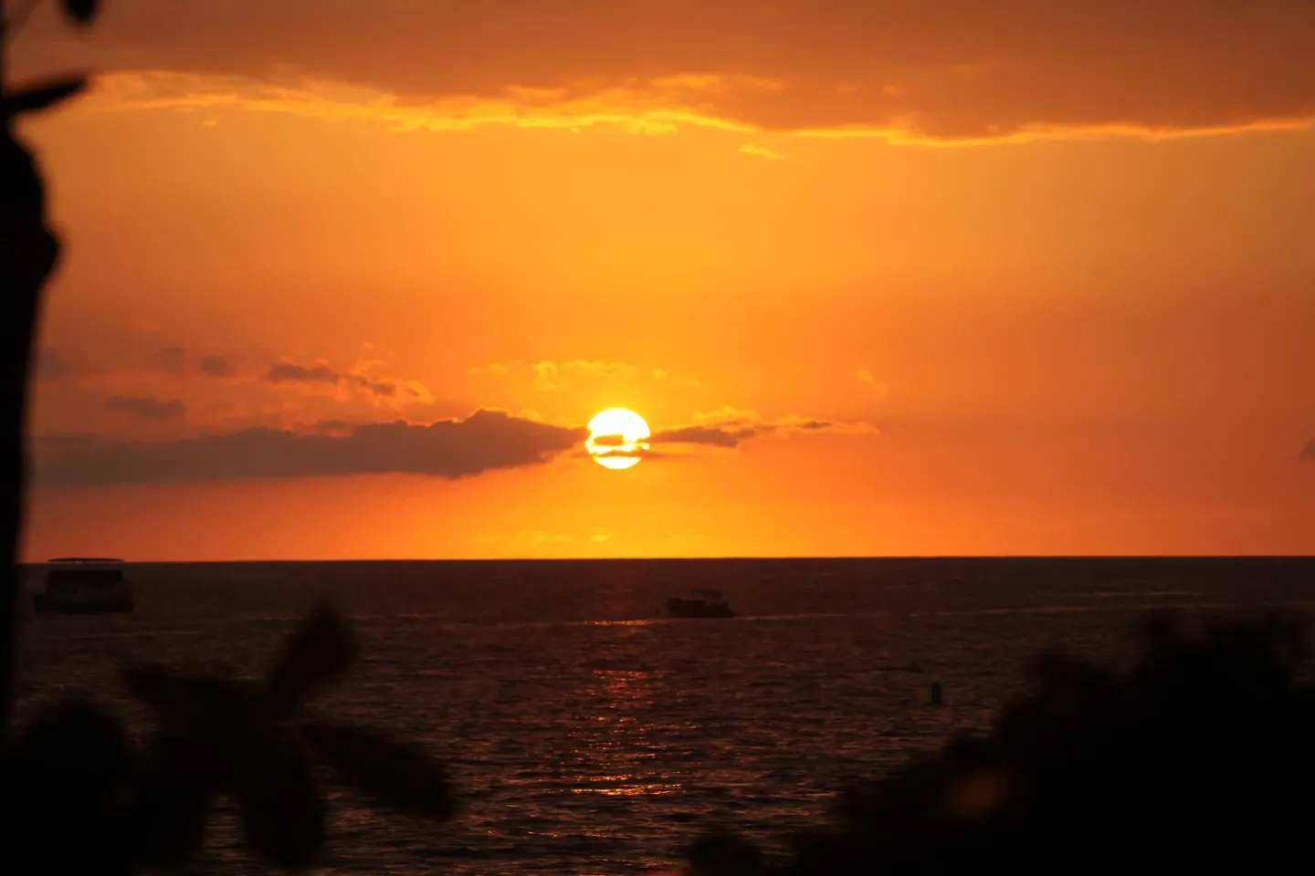 Orange sunset over the ocean with boat silhouettes near Royal Kona Resort.