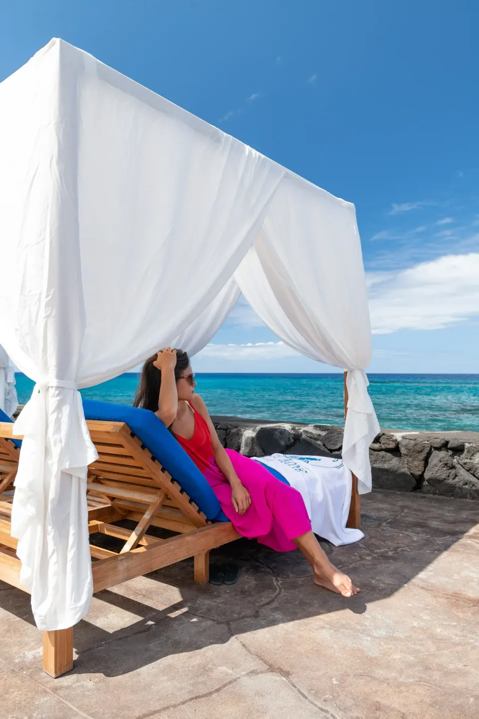 Canopied oceanfront daybed with a guest relaxing at Royal Kona Resort.