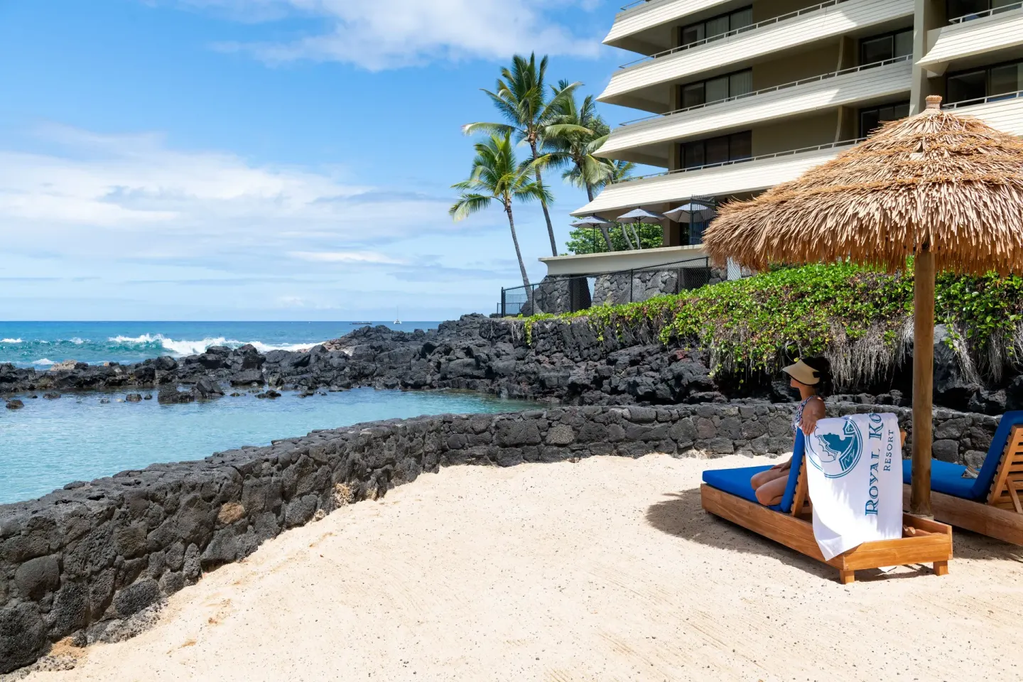 Lounge chairs face the ocean lagoon and resort tower at Royal Kona Resort.