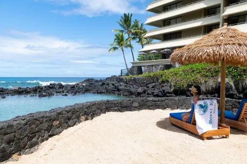 Lounge chairs face the ocean lagoon and resort tower at Royal Kona Resort.