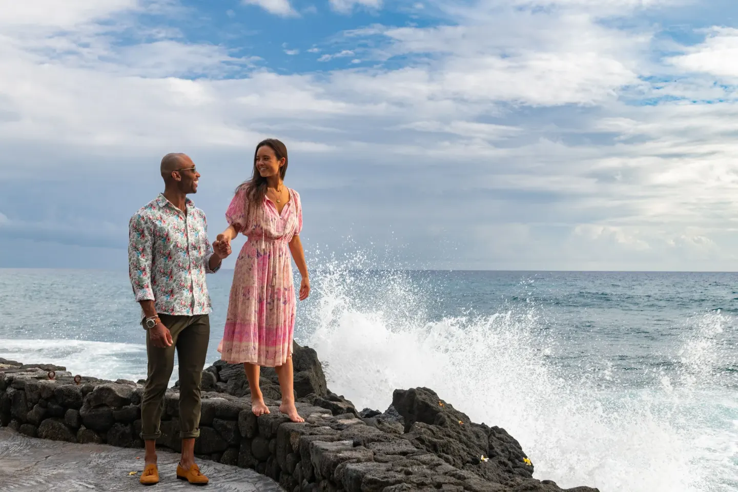 Couple stands by lava rocks as waves splash beside Royal Kona Resort.