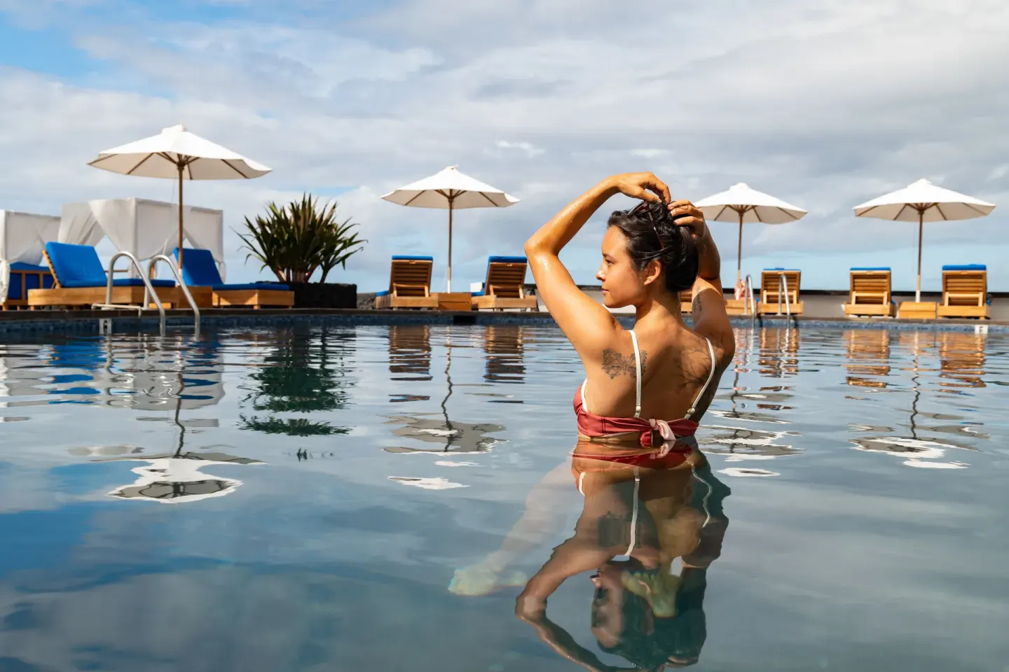 Guest standing in the pool with lounge chairs and umbrellas at Royal Kona Resort.