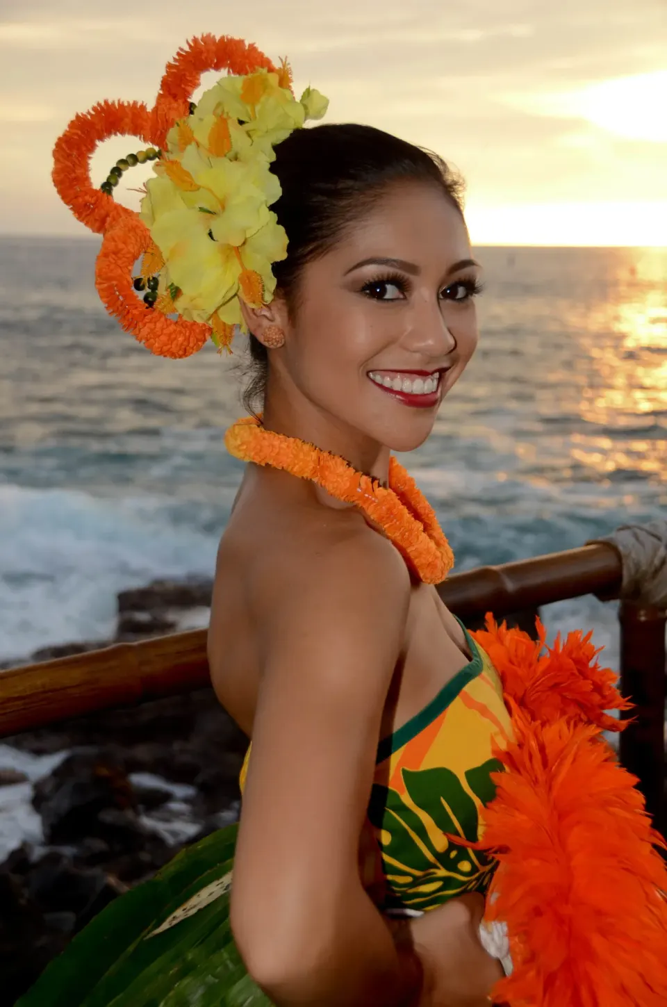 Hula performer in floral adornments posing by the ocean at sunset at Royal Kona Resort.