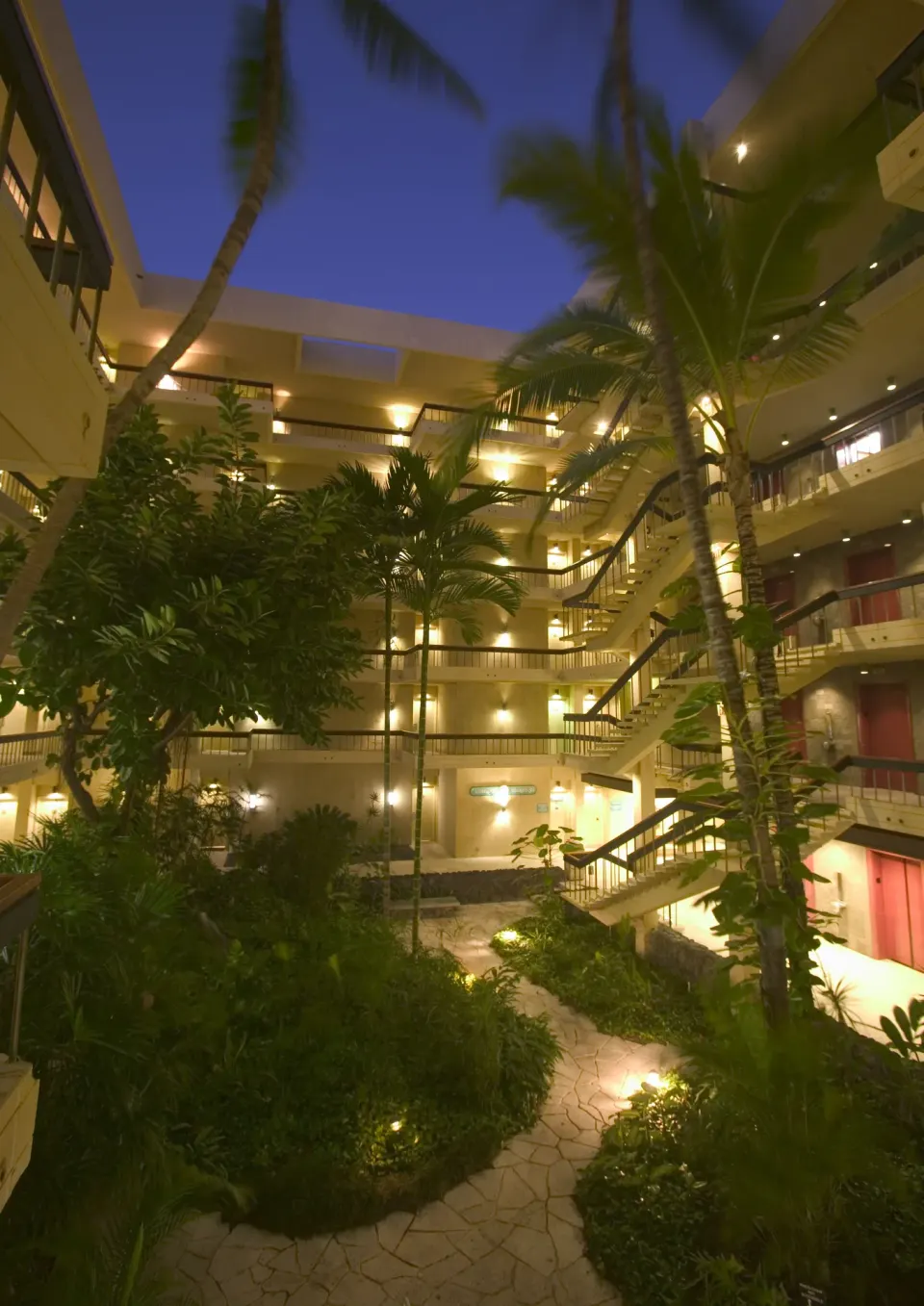 A lit tropical courtyard with palms and exterior walkways at Royal Kona Resort.