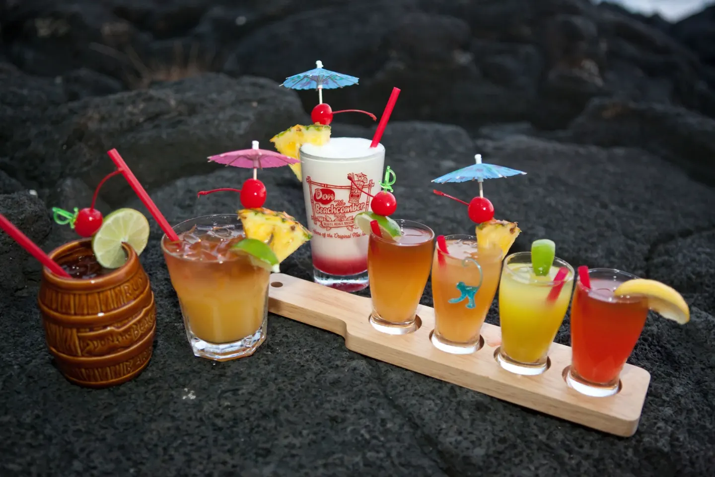 Assorted tropical cocktails with umbrellas and fruit garnishes on black lava rock at Royal Kona Resort.