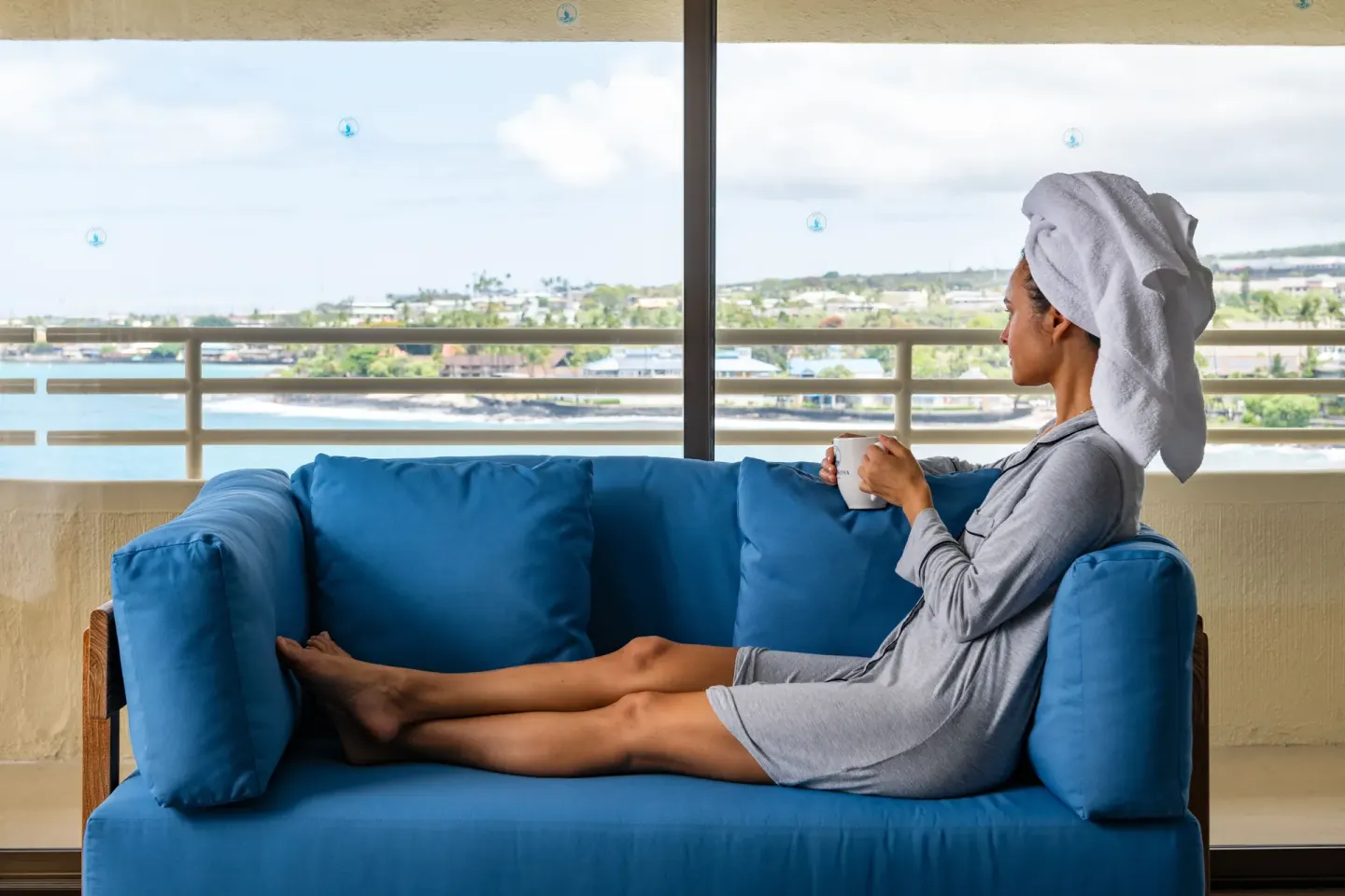 Guest relaxing on a blue sofa by the ocean view window at Royal Kona Resort.