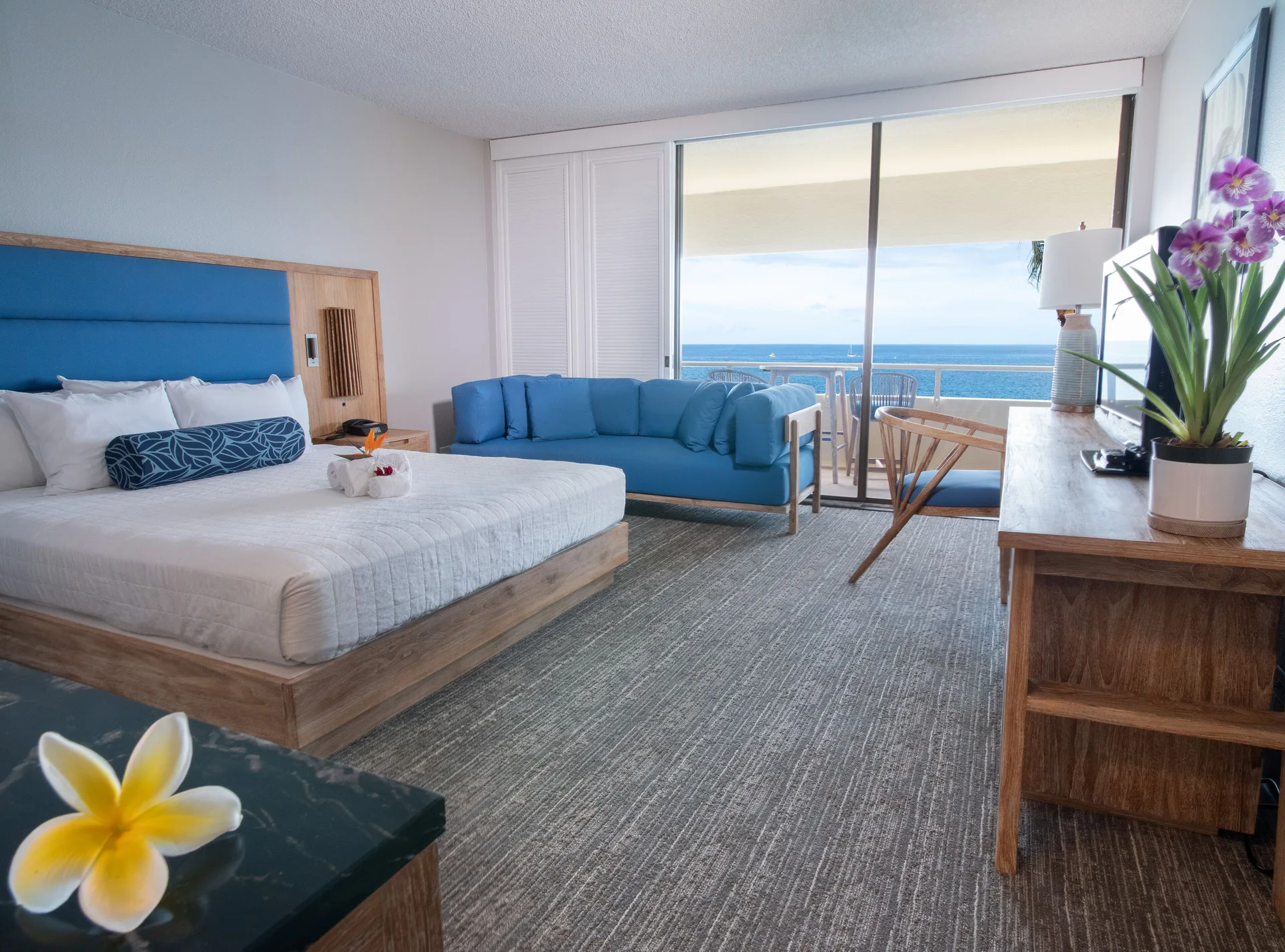 Oceanfront king room with blue sofa and balcony view at Royal Kona Resort.