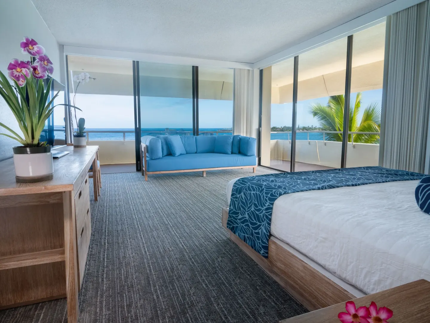 Corner oceanfront guest room with king bed, blue sofa, and ocean-facing windows at Royal Kona Resort.