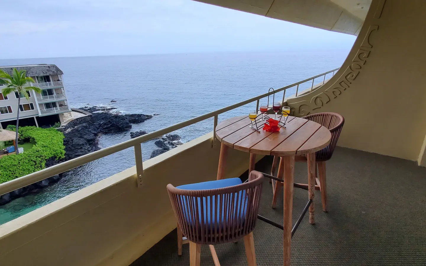 Oceanfront room lanai with table, two chairs, drinks, and coastline view at Royal Kona Resort.