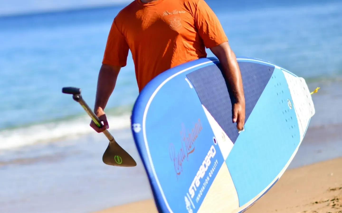 Person carrying a paddleboard and paddle on the beach at Royal Lahaina Resort & Bungalows.