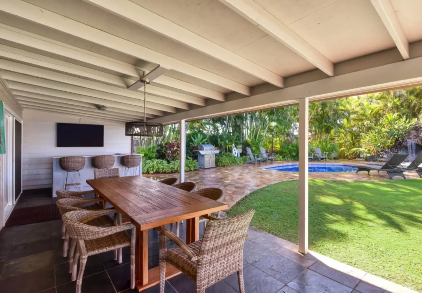 Covered patio with dining table, bar stools, lawn, and pool at Royal Lahaina Resort & Bungalows.