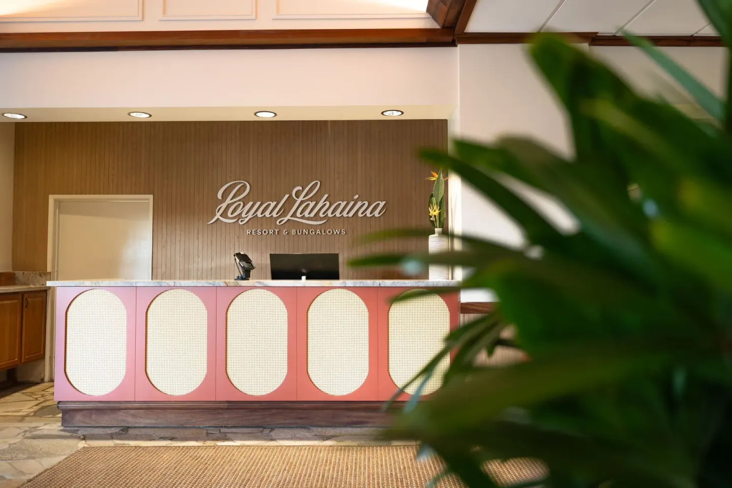 Lobby reception desk with Royal Lahaina Resort & Bungalows sign and tropical plant in the foreground.