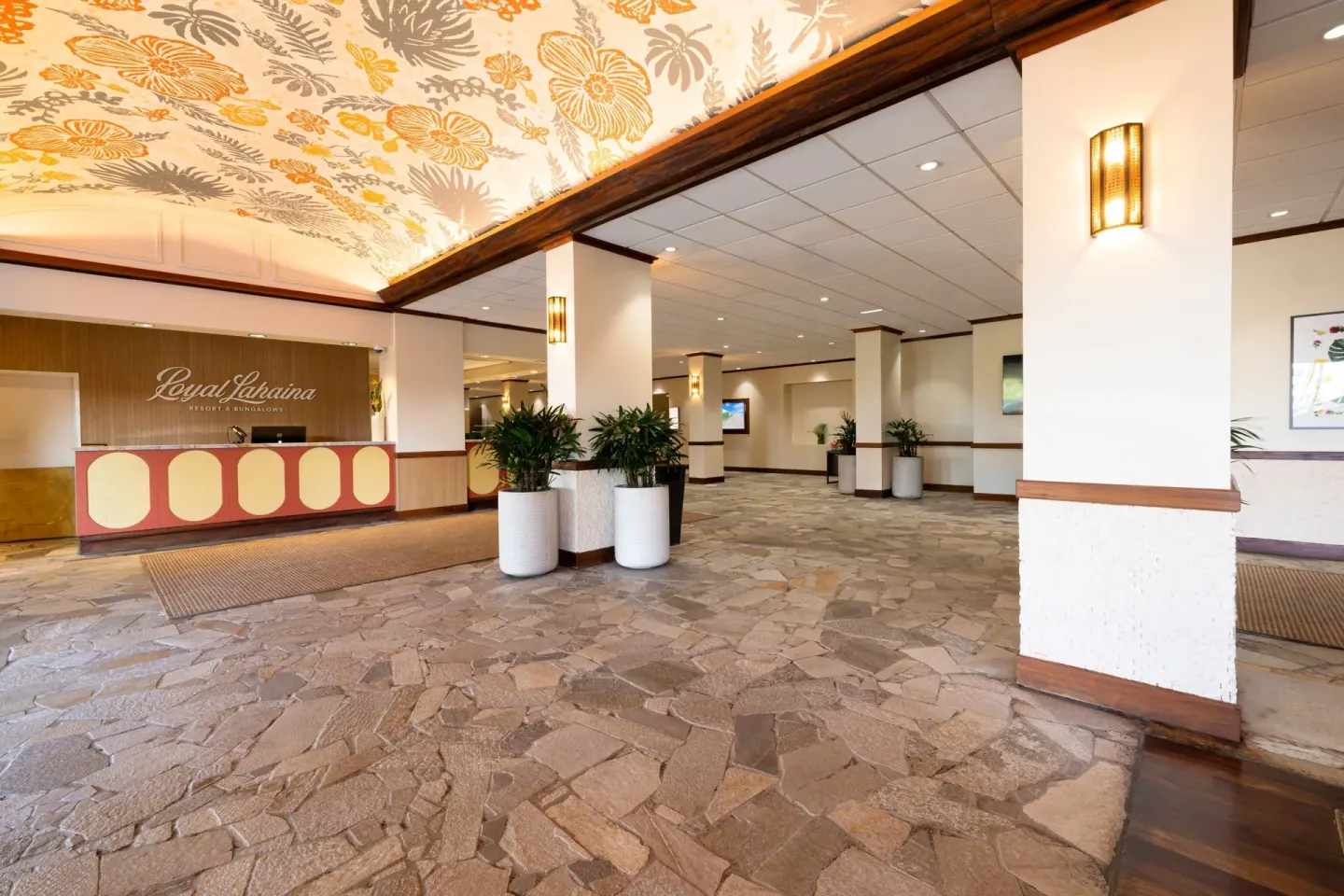 Open lobby at Royal Lahaina Resort & Bungalows with reception desk, stone floor, and floral ceiling.