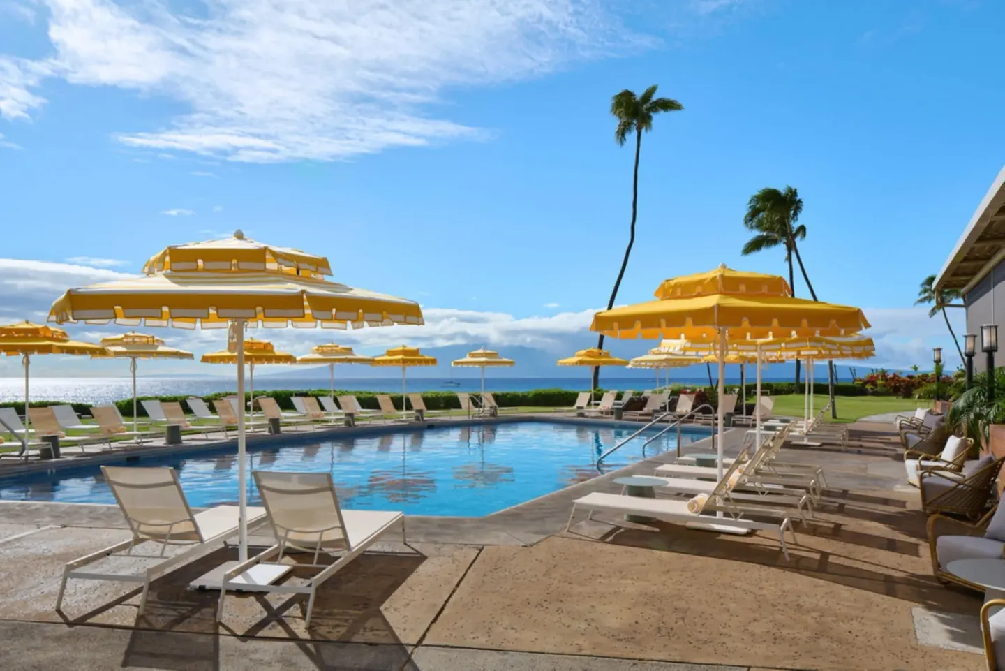 Pool deck with yellow umbrellas and ocean beyond at Royal Lahaina Resort & Bungalows.
