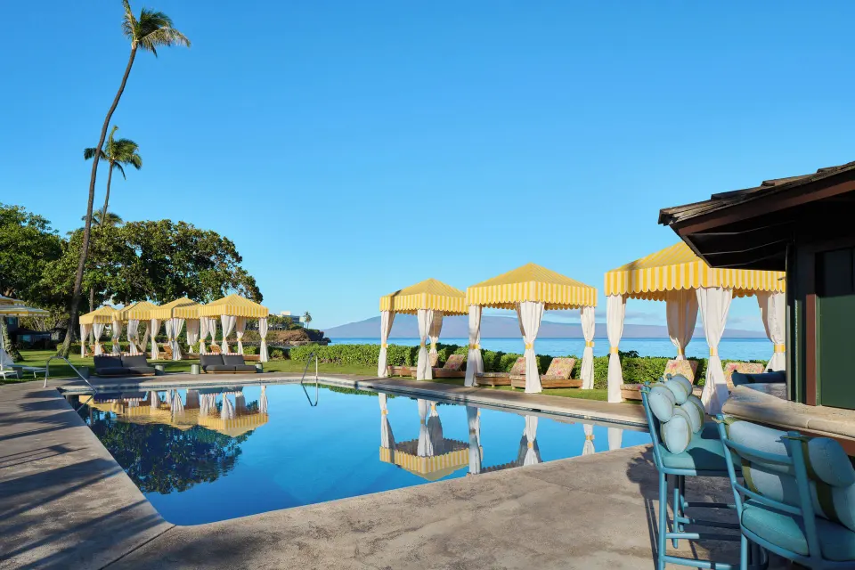Pool at Royal Lahaina Resort & Bungalows with yellow cabanas, lounge seating, and ocean beyond.