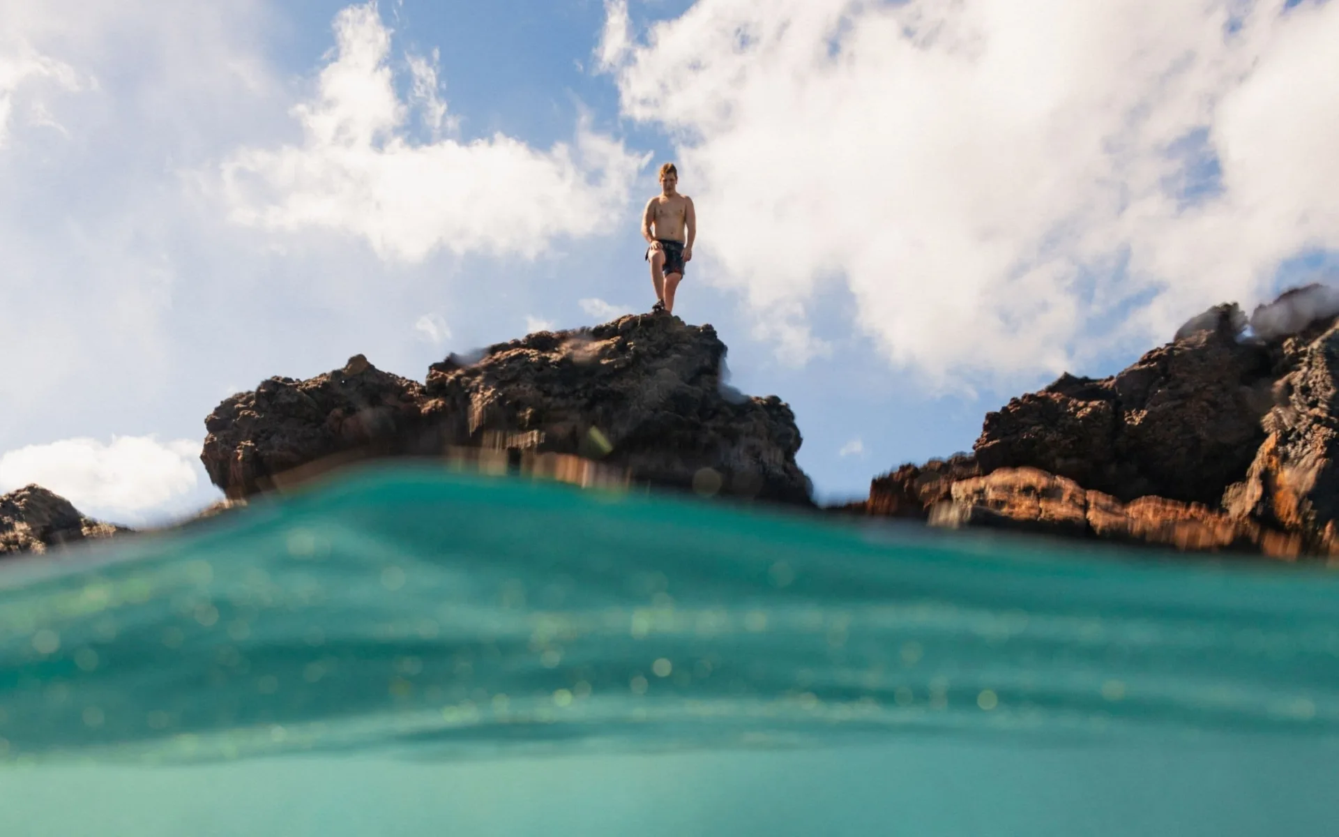 Person standing on dark ocean rocks above turquoise water at Royal Lahaina Resort & Bungalows.