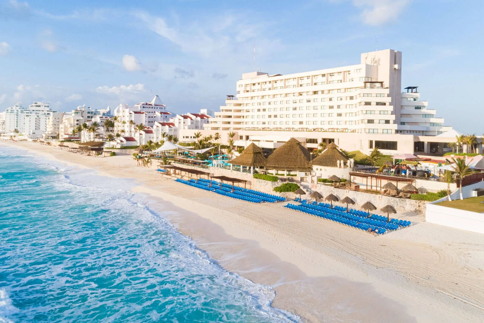 Beachfront view of Royal Solaris Cancun with turquoise surf, palapas, and blue loungers.