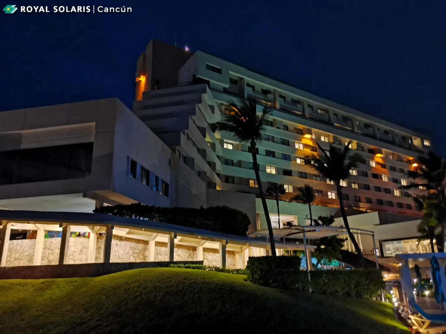 Night exterior of Royal Solaris Cancun with palms, lit rooms, and logo overlay.