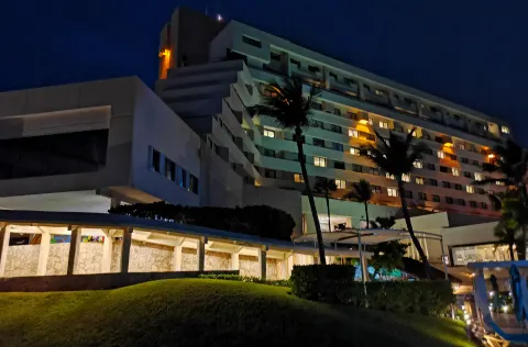 Night exterior of Royal Solaris Cancun with lit windows, palms, and landscaped grounds.