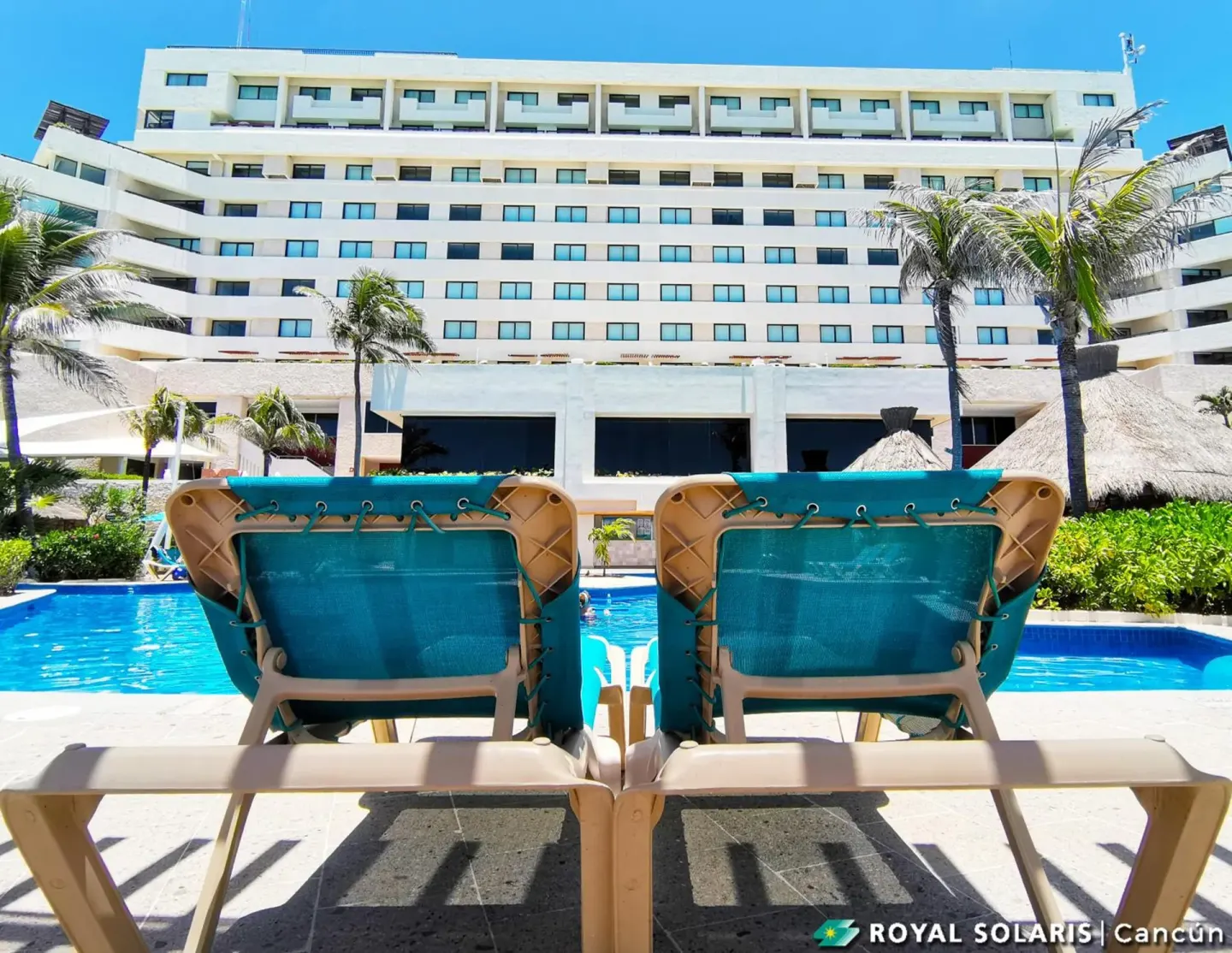 Pool loungers facing the Royal Solaris Cancun building on a sunny day.