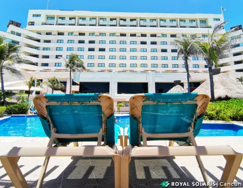 Pool loungers facing the Royal Solaris Cancun building on a sunny day.
