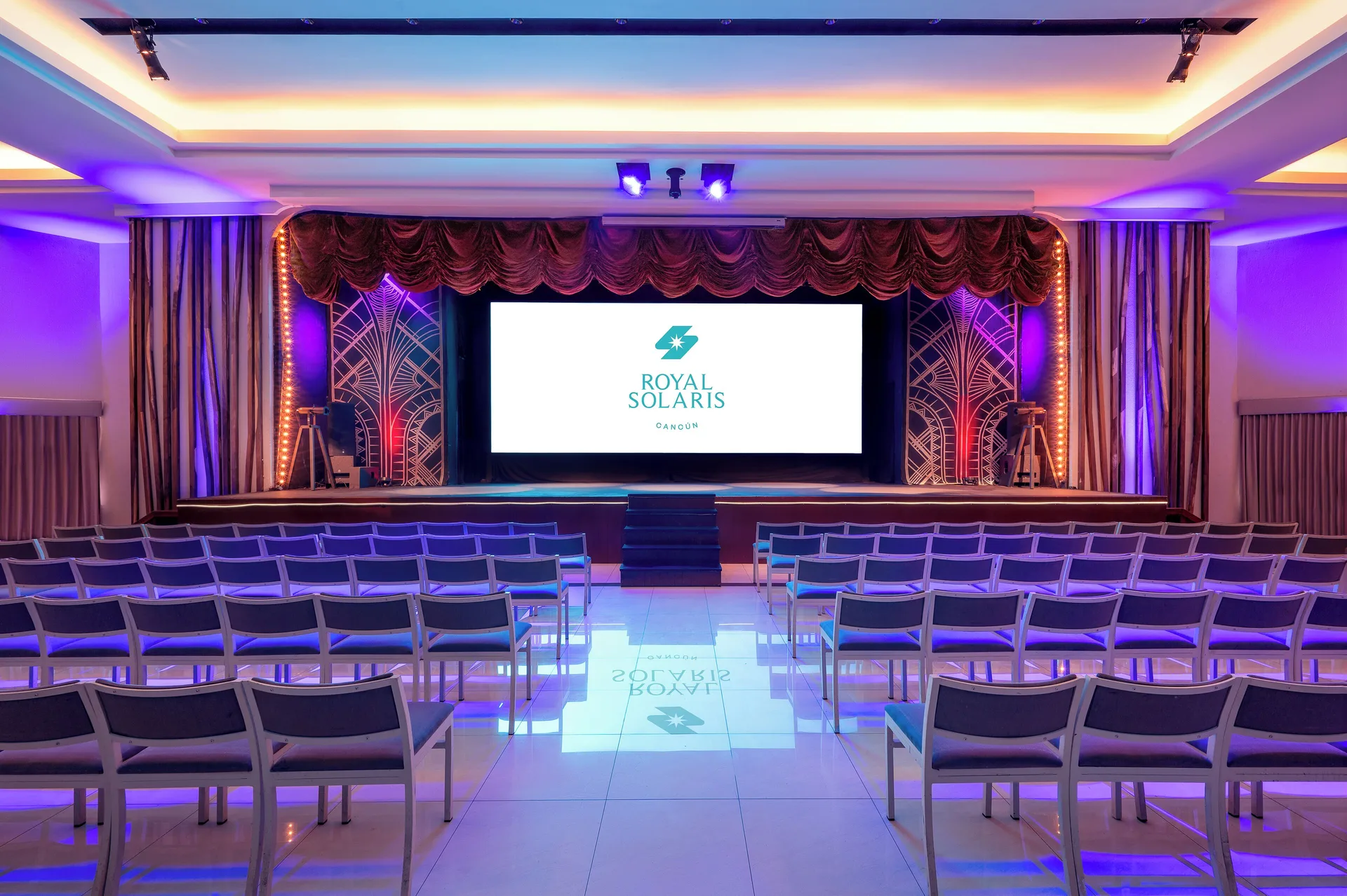 Theater seating faces a lit stage and screen at Royal Solaris Cancun.