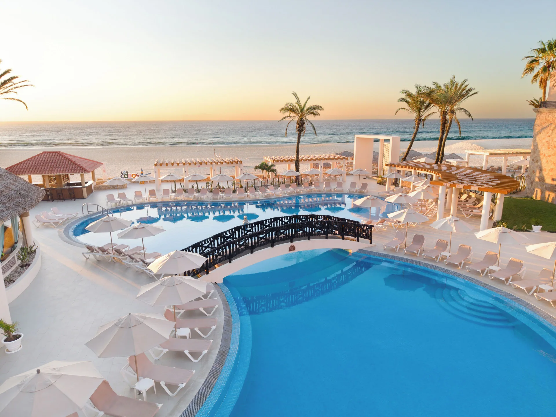 Beachside pools with white loungers and ocean sunset at Royal Solaris Los Cabos & Spa.