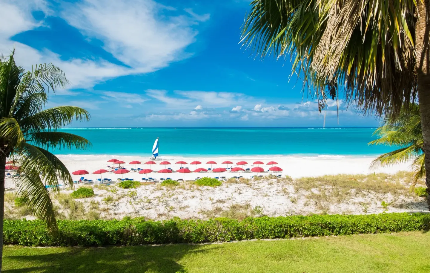 Beachfront with red umbrellas and turquoise water at Royal West Indies Resort.