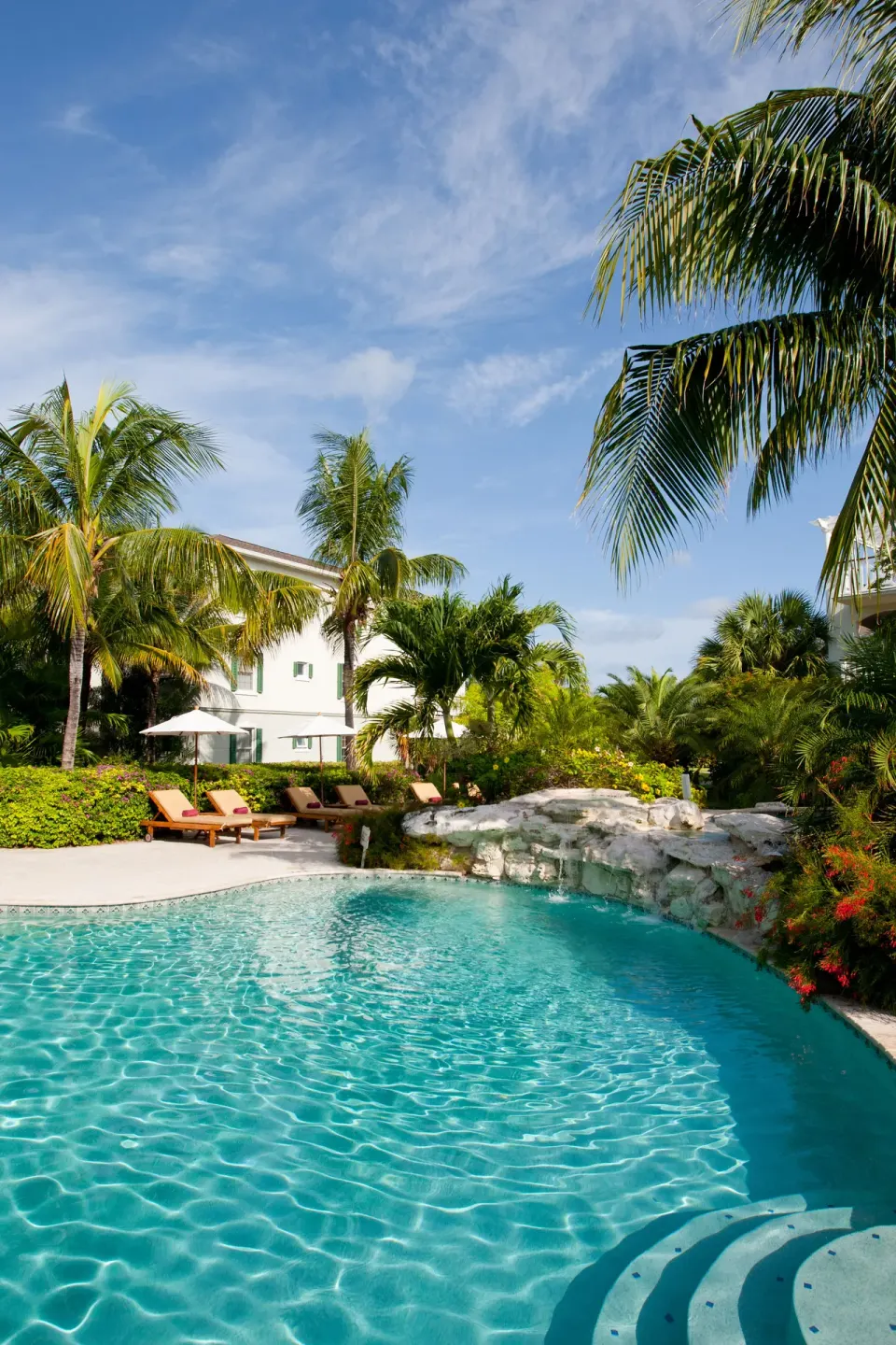 Curved pool with rock feature, palms, and loungers at Royal West Indies Resort.